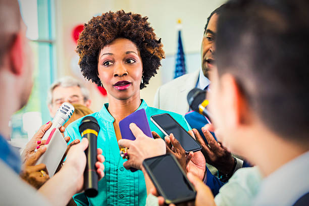 Concerned woman confronted by journalists Concerned African American woman in teal is confronted by journalists with phones and microphones. woman press conference stock pictures, royalty-free photos & images