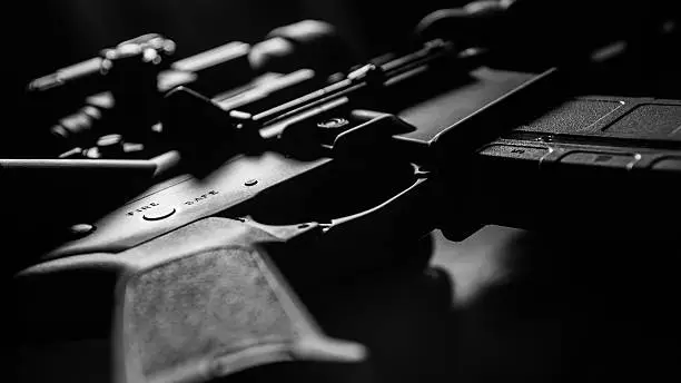 High contrast black and white AR-15 close-up with selective focus on Safe / Fire receiver stamping.