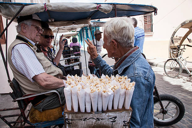 Camagüey, Cuba, March 16, 2013: A Cuban street vendor sells churros to two tourists riding in a bicitaxi.