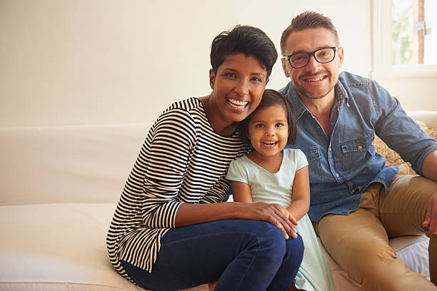 Happiness comes from family Cropped portrait of a family of three sitting on their living room sofa multiracial person stock pictures, royalty-free photos & images