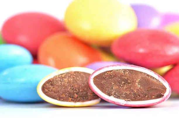 Close-up of halved red and yellow smarties with chocolate filling and blue, purple, yellow smarties in background