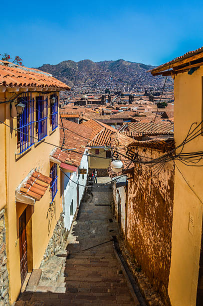 Cusco, Peru - August 22, 2014: A narrow street in central Cusco with old colonial architecture, cobblestone roads, and some people either walking. Photo taken during a warm day.