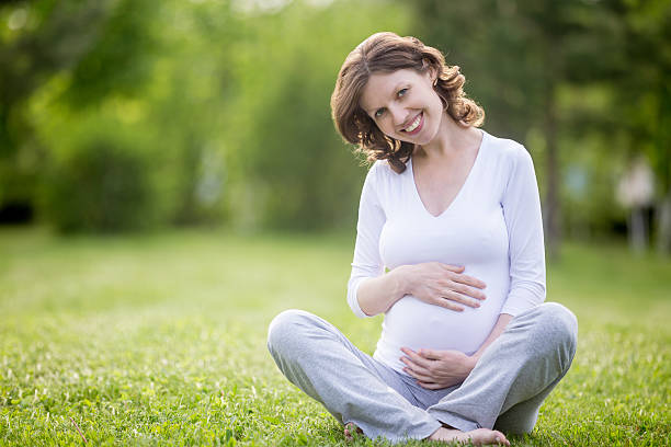 sorridente futura mãe sentar de pernas cruzadas na relva gramado - relaxation exercise child mother human pregnancy imagens e fotografias de stock