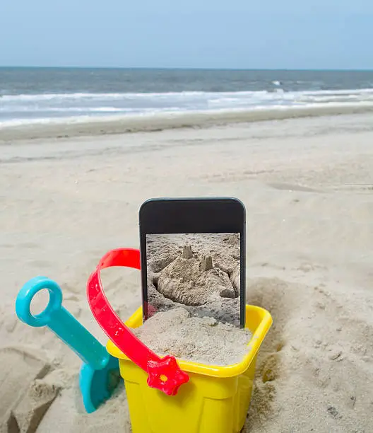 Photo of Empty beach with sand castle on smartphone with clipping path