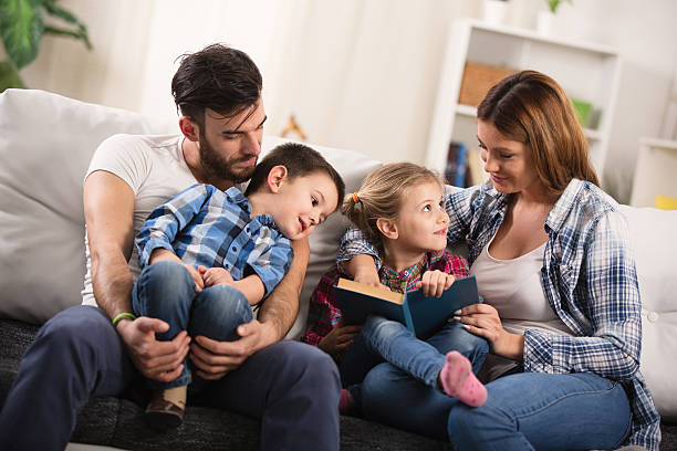 istock Mother and father with children sitting on sofa reading book. 534410352