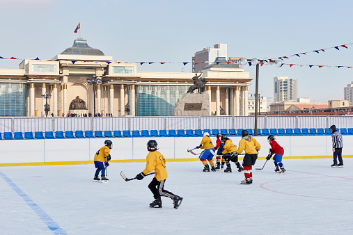 Ulan Bator, Mongolia - January 25, 2015: young mongolians engaged in a ice hockey match in Chinggis Square. In the background the Monument to Chinggis Khan.