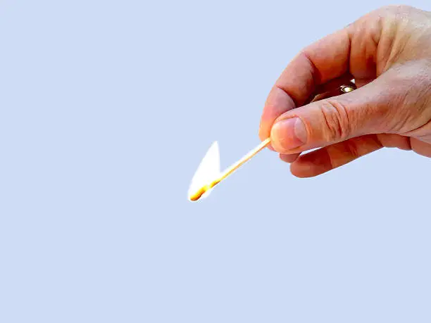 Burning match held by 2 fingers isolated on light background
