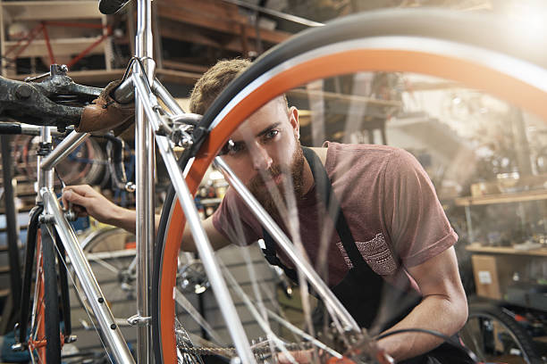 Nothing replaces hard work and diligent focus Shot of a handsome young bicycle mechanic working on a customer's bicycle bicycle shop stock pictures, royalty-free photos & images