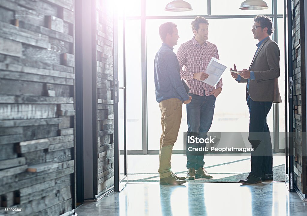 Hallway brainstorming Shot of male coworkers talking while standing in front of a window in an office 2015 Stock Photo