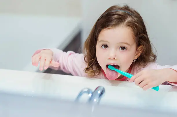 Photo of Little girl in pink pyjamas in bathroom brushing teeth
