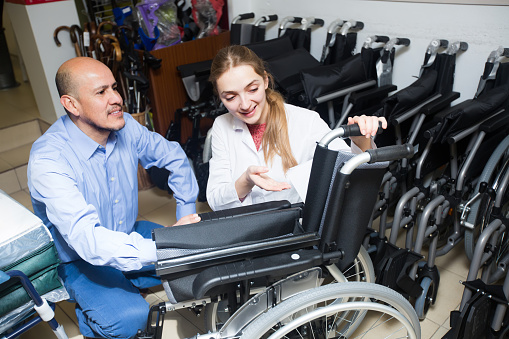 Smiling  female consultant offering manual wheelchairs to male customer in orthopaedic store