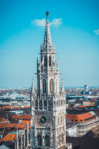 Architectural Close Up of Gothic Style New City Hall Clock Tower with Overview of Rooftops of City of Munich on Sunny Day with Bright Blue Sky