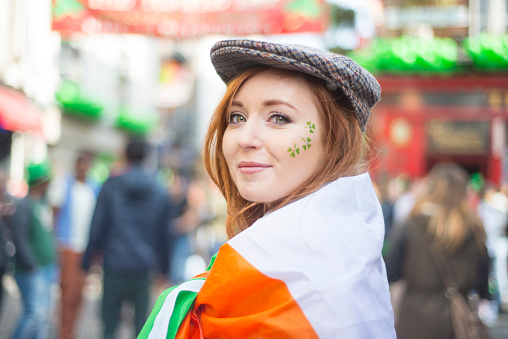 Smiling red haired Irish girl with face painted and the Irish flag and tweed cap in Temple Bar, Dublin, Ireland