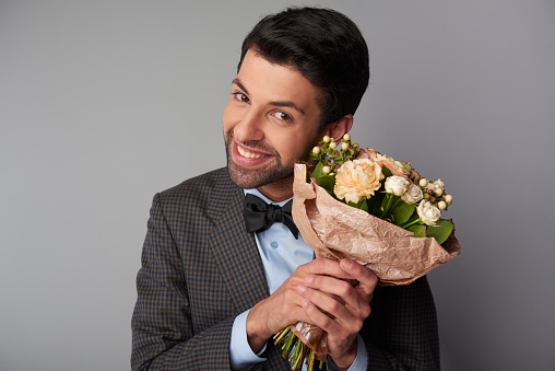 Smiling young man wearing a tweed jacket and black bow tie holding nice bouquet of roses and looking at camera. Concept for Valentine's Day