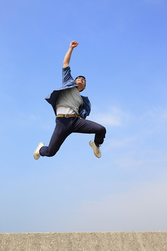 Happy College student man run and jump with blue sky background, full length, asian male