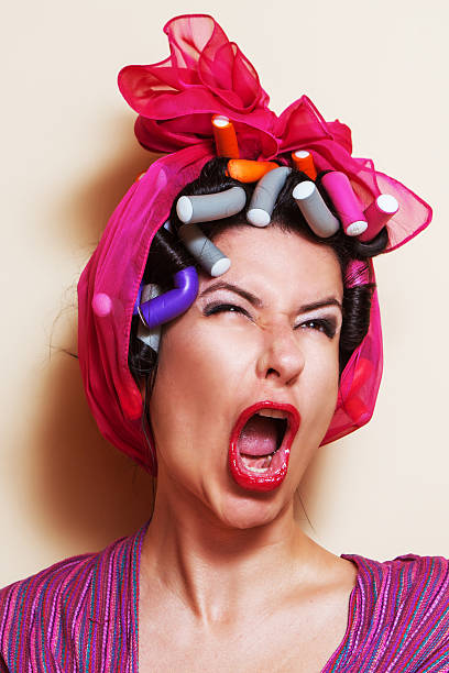 Close-up of a young woman with hair curlers making a grimace Close-up of a young woman with hair curlers making a yelling grimace sour face stock pictures, royalty-free photos & images