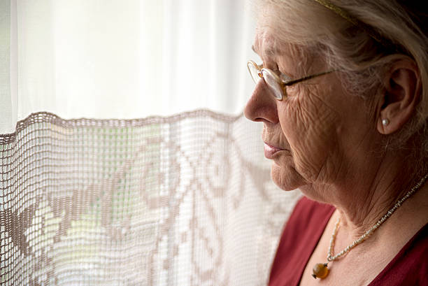 An elderly lady sitting near the window in the kitchen An elderly lady sitting near the window in the kitchen, Lovely grandmother looking in a window. grandmother real people front view head and shoulders stock pictures, royalty-free photos & images