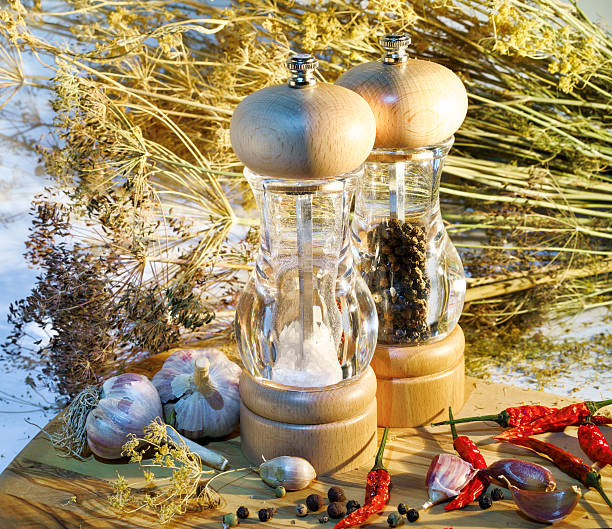 salt and pepper mill with ingredients around on wooden cutting board