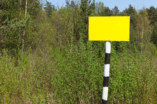 Empty yellow sign board on striped black and white pole over summer nature background