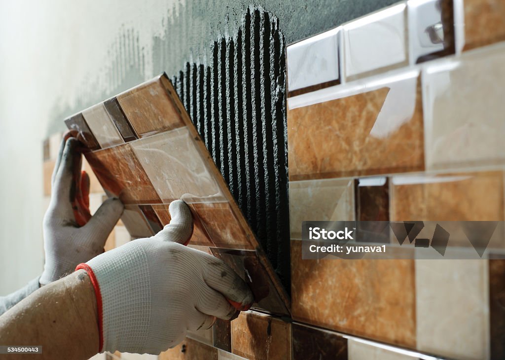 Laying Ceramic Tiles. Laying Ceramic Tiles. Tiler placing ceramic wall tile in position over adhesive Tile Stock Photo