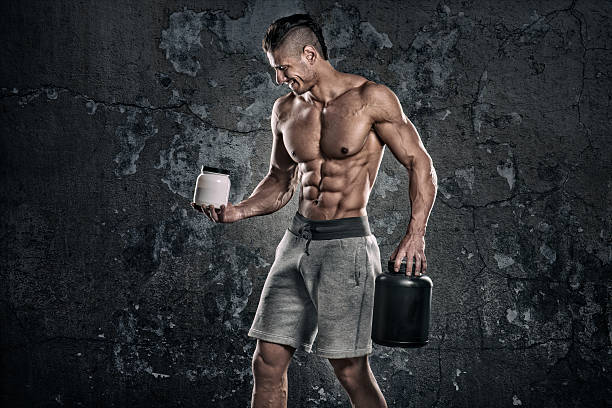 Bodybuilder with supplements Studio portrait of shirtless male fitness athlete perfectly shaped and muscle toned wearing grey shorts and holding cans of supplements. bodybuilding supplement stock pictures, royalty-free photos & images
