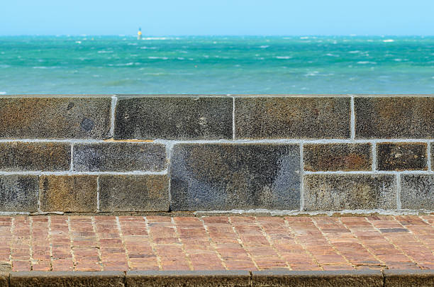 A slightly turbulent sea laps over a concrete wall and steps that lead into the sea, on a sunny day.
