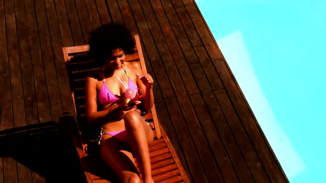 Gorgeous woman in pink bikini drinking cocktail by swimming pool