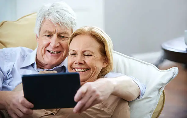 Shot of a happy elderly couple watching something on a digital tablet while relaxing on their sofa