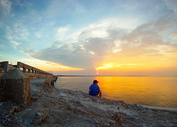 Young man sitting on beach at sunset stock photo