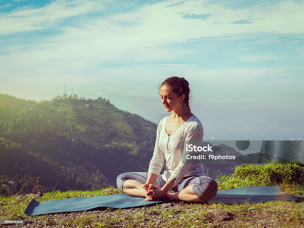 Sporty fit woman practices yoga asana Baddha Konasana outdoors Vintage retro effect hipster style image of sporty fit woman practices yoga asana Baddha Konasana - bound angle pose outdoors in HImalayas mountains in the morning with sky. Himachal Pradesh, India Activity Stock Photo