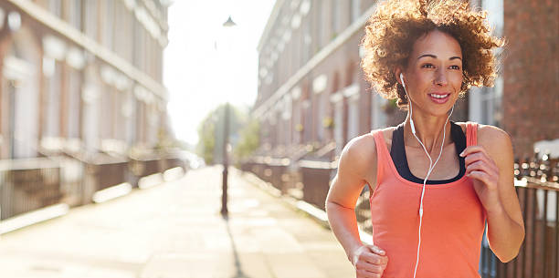 city jog a young woman running in a street on her morning or evening run . She is backlit by a rising low sun , and is pictured staring ahead with determination , before heading off on her morning jog.She is wearing a vest top , trainers and leggings , and earphones. The sun is rising at dawn behind her or setting at sunset . Lens flare streaks across the frame . liverpool one stock pictures, royalty-free photos & images