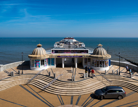 Cromer, Norfolk, England - May 5, 2016: A few people enjoying the sun on and around Cromer Pier in Cromer, Norfolk, eastern England on a day in early May. Cromer is famous for its pier and Pavilion Theatre shows and has been voted ‘Pier of the Year 2015’ by the National Piers Society.
