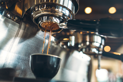 Fresh and hot espresso coffee pours from a portafilter on a nice chrome espresso machine.  Horizontal image.