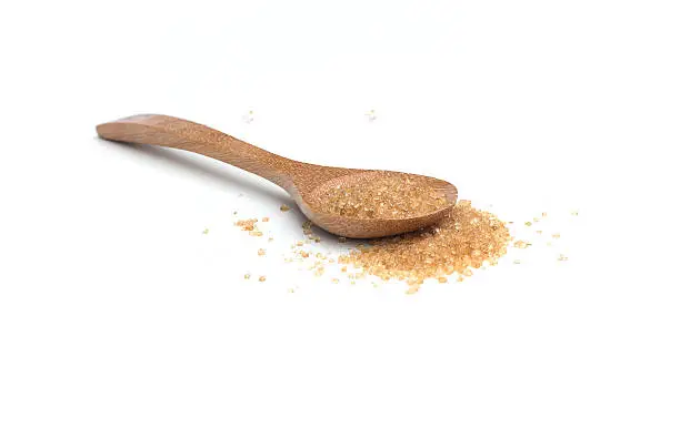 Heap of organic brown cane sugar with wooden spoon isolated on white background
