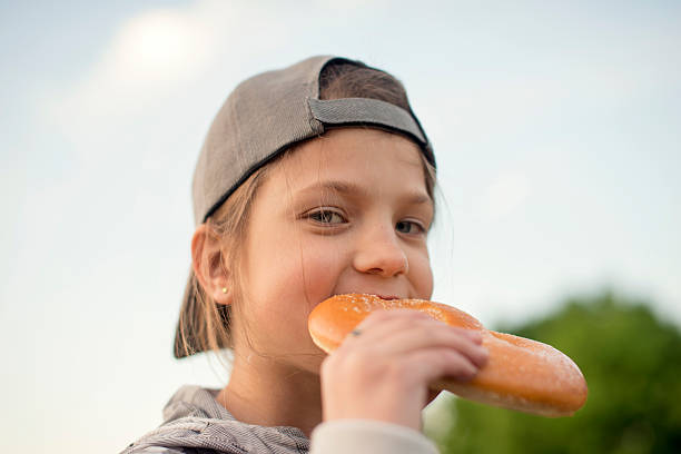 Young cute european girl in t-shirt is eating unhealthy food like hot dog and chips at sunny day