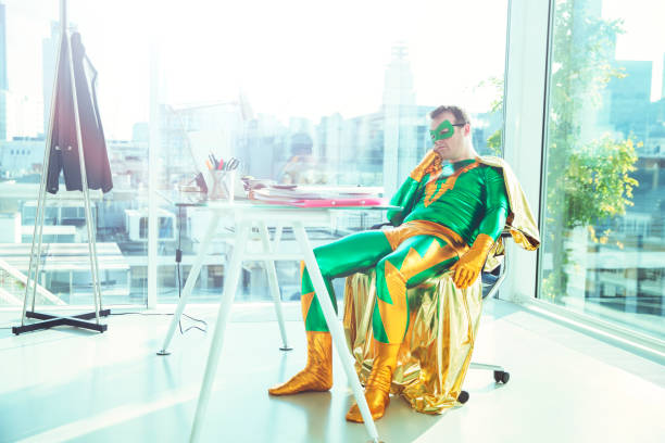 bored superhero slouching at desk in office - superhero humor men cape imagens e fotografias de stock