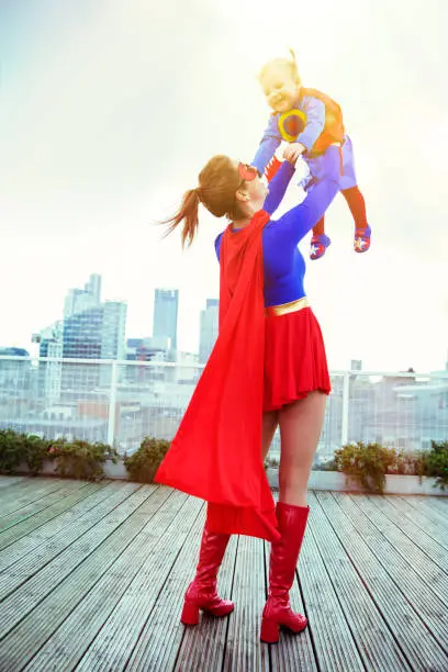 Photo of Superhero mother playing with daughter on city rooftop