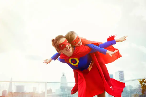 Photo of Superhero mother and daughter playing on city rooftop