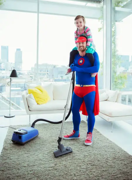 Photo of Superhero father vacuuming and carrying daughter on shoulders