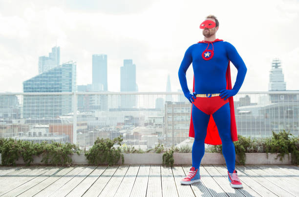superhero standing with hands on hips on city rooftop - superhero humor men cape imagens e fotografias de stock