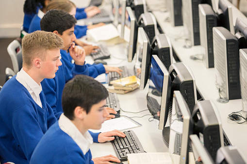 Group of male and female high school students does research in the high school computer lab. The teenage friends enjoy learning and studying together.