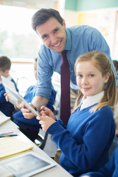 istock Portrait of male teacher with his pupils in classroom using tablet pc 534575875