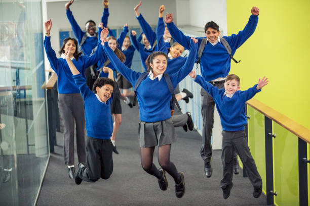 enthusiastic high school students wearing school uniforms smiling and jumping in school corridor - onderwijs fotos stockfoto's en -beelden