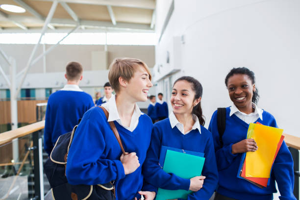 estudiantes sonrientes con uniformes escolares caminando por el pasillo de la escuela - uniforme de colegio fotografías e imágenes de stock
