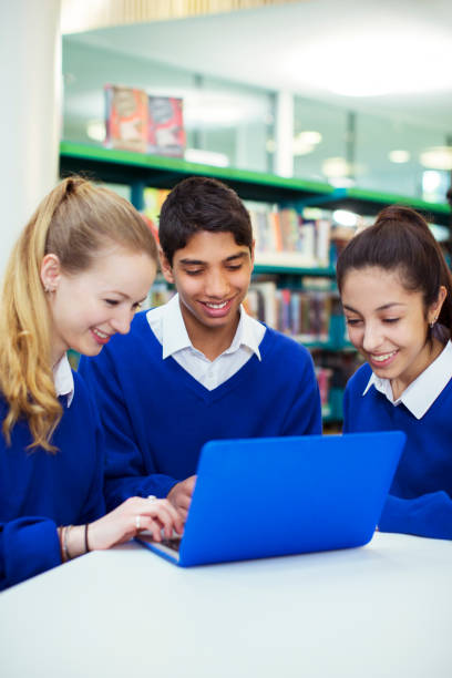 Three cheerful students working with laptop in library  teenagers only teenager multi ethnic group student stock pictures, royalty-free photos & images