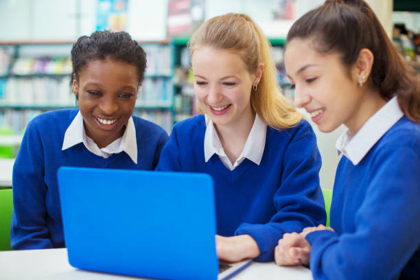 Three smiling female students wearing blue school uniforms working on laptop in library  teenagers only teenager multi ethnic group student stock pictures, royalty-free photos & images