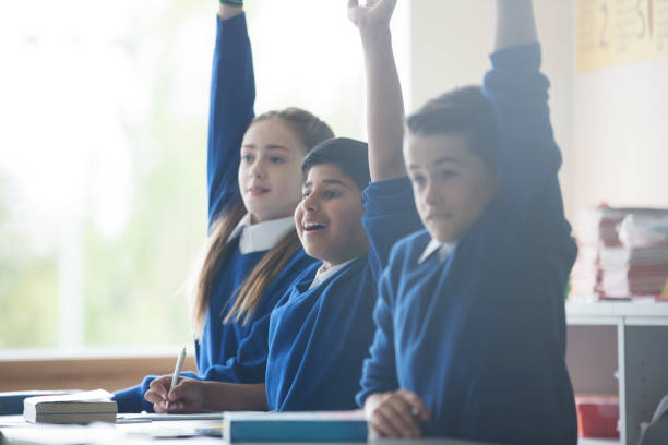 istock Primary school children in classroom raising arms 534576493