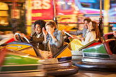 Group of friends having fun on bumper car ride in amusement park