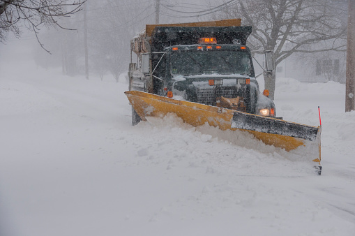 Weymouth, MA, USA-January 27, 2015: A large truck with a yellow plow pushes through snow as it plows a street during a New England blizzard.