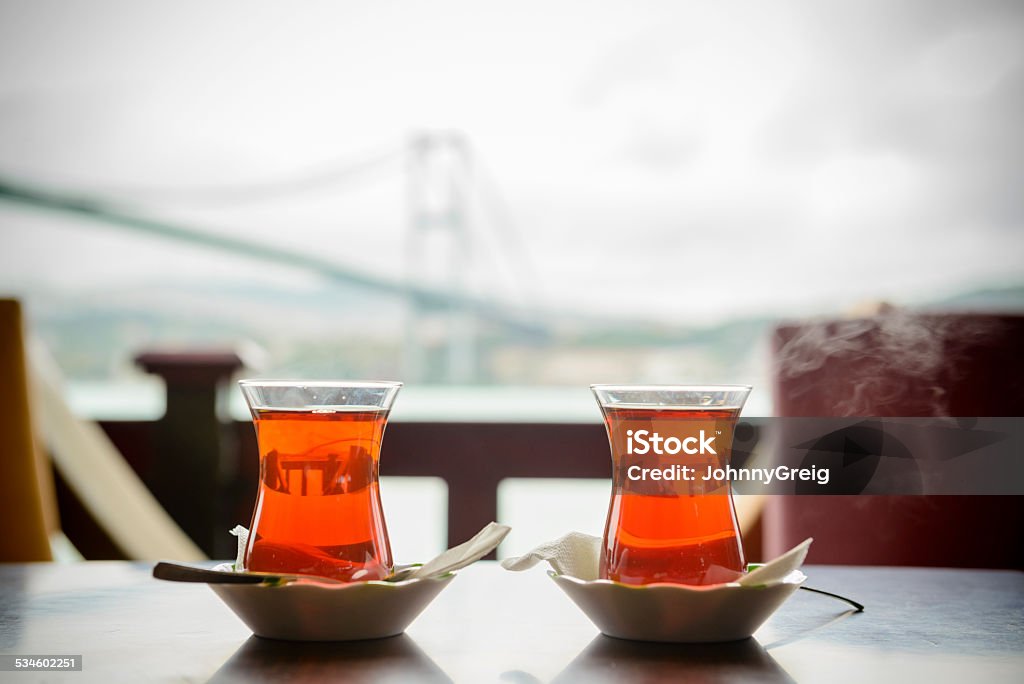 Traditional Turkish Tea in Istanbul Two cups of Turkish tea in tulip glasses at cafe table with Bosphorous bridge in backgroundTwo cups of Turkish tea in tulip glasses at cafe table with Bosphorous bridge in background Tea - Hot Drink Stock Photo